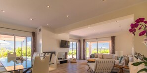 A spacious living area with a glass dining table, a sofa, and a TV mounted on the wall.