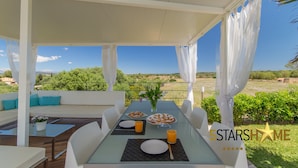 A covered outdoor dining area with a table set for two, a sofa, and a view of the landscape. - The Land, Villa-Finca 5StarsHome Mallorca (San Jordi)