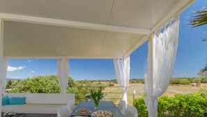 Uma área de refeições ao ar livre coberta, com uma mesa posta para dois, um sofá e vista para a paisagem.