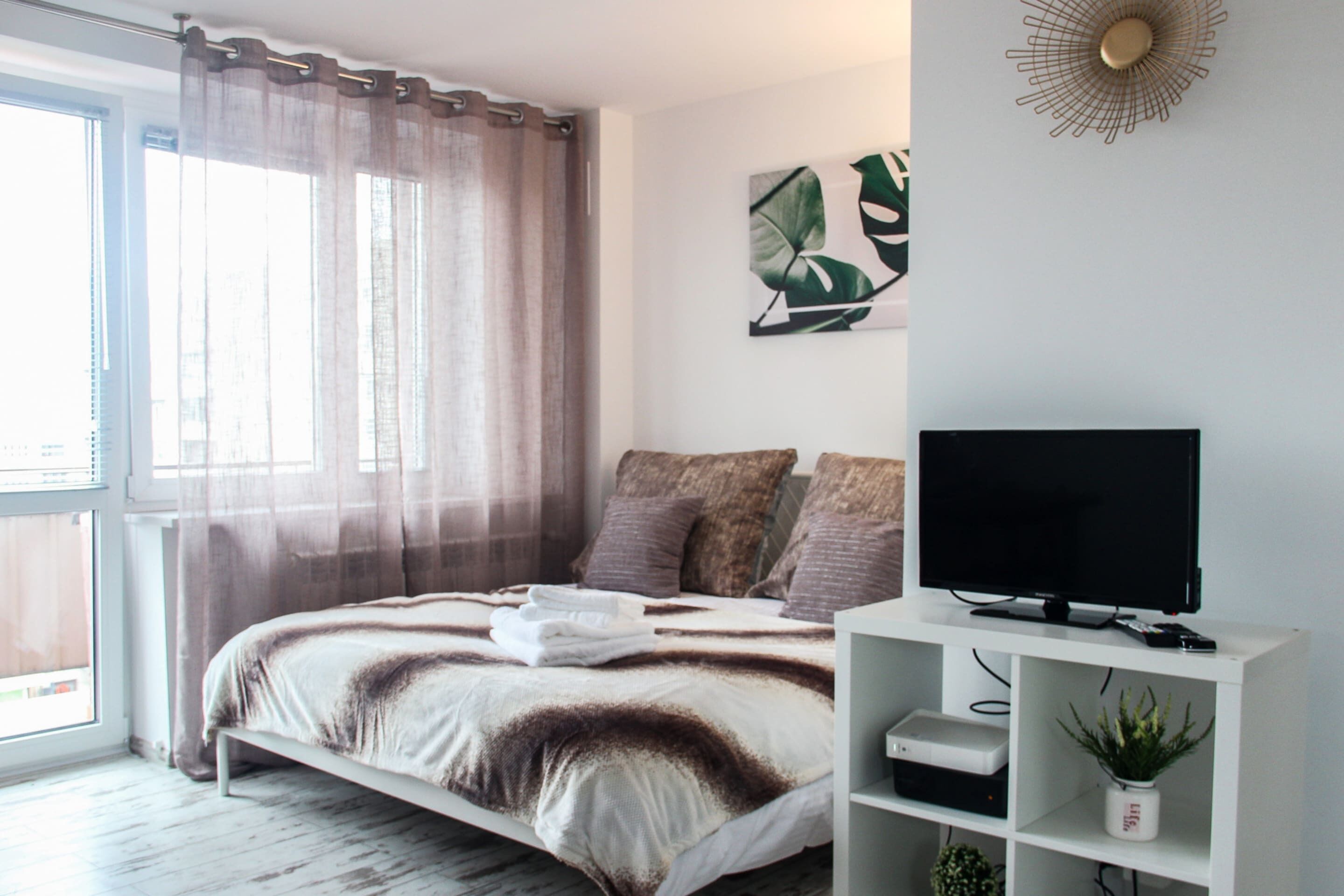 Ein modernes Schlafzimmer mit einem Bett, einem Fernseher und einem Regal mit einer Pflanze.