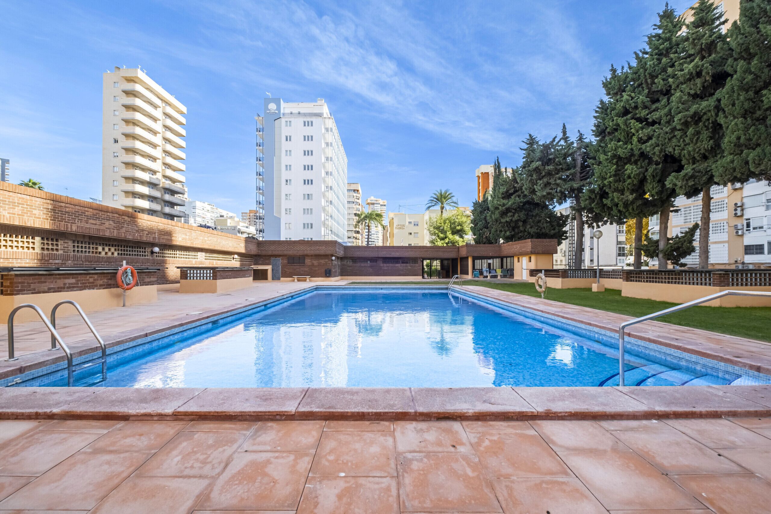 Une piscine dotée d’une terrasse carrelée, entourée d’immeubles et d’arbres imposants.