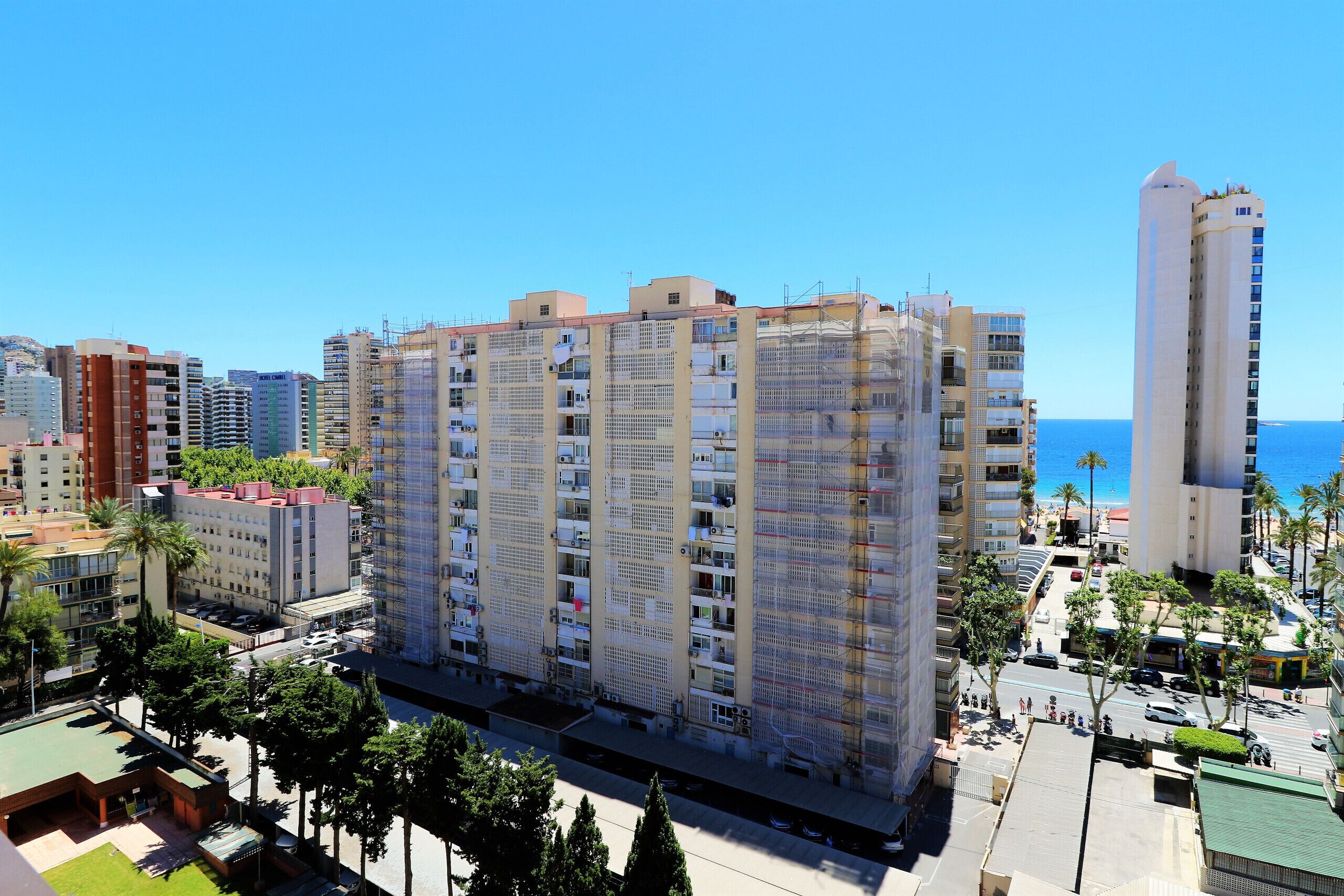 A multi-story residential building with balconies, located near a coastal area with visible blue water.
