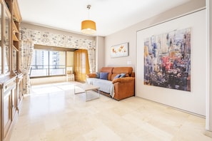 A living room with a sofa, a coffee table, a cityscape painting, and a window with curtains.