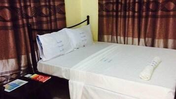 A neatly made bed with white linens, a rolled towel, and a small table with a book and a magazine.