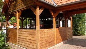 Eine Holzpergola mit Ziegeldach, ausgestattet mit überdachter Sitzgelegenheit und großen Fenstern.