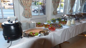 Ein Buffet mit verschiedenen Speisen, einer Kaffeemaschine und Blick auf die Straße durch das Fenster.