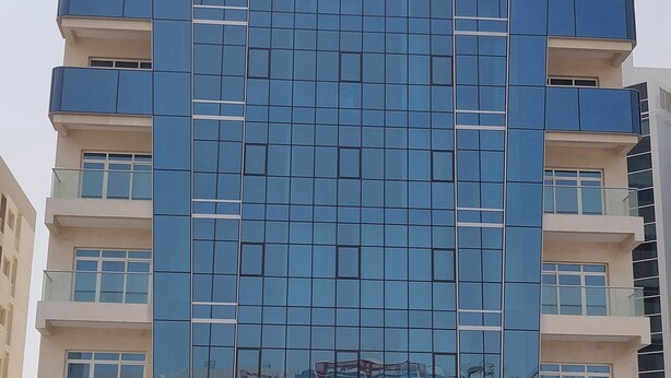 A modern hotel building with a glass facade, multiple balconies, and a sign indicating it is Tulip Al Barsha Hotel Apartments.