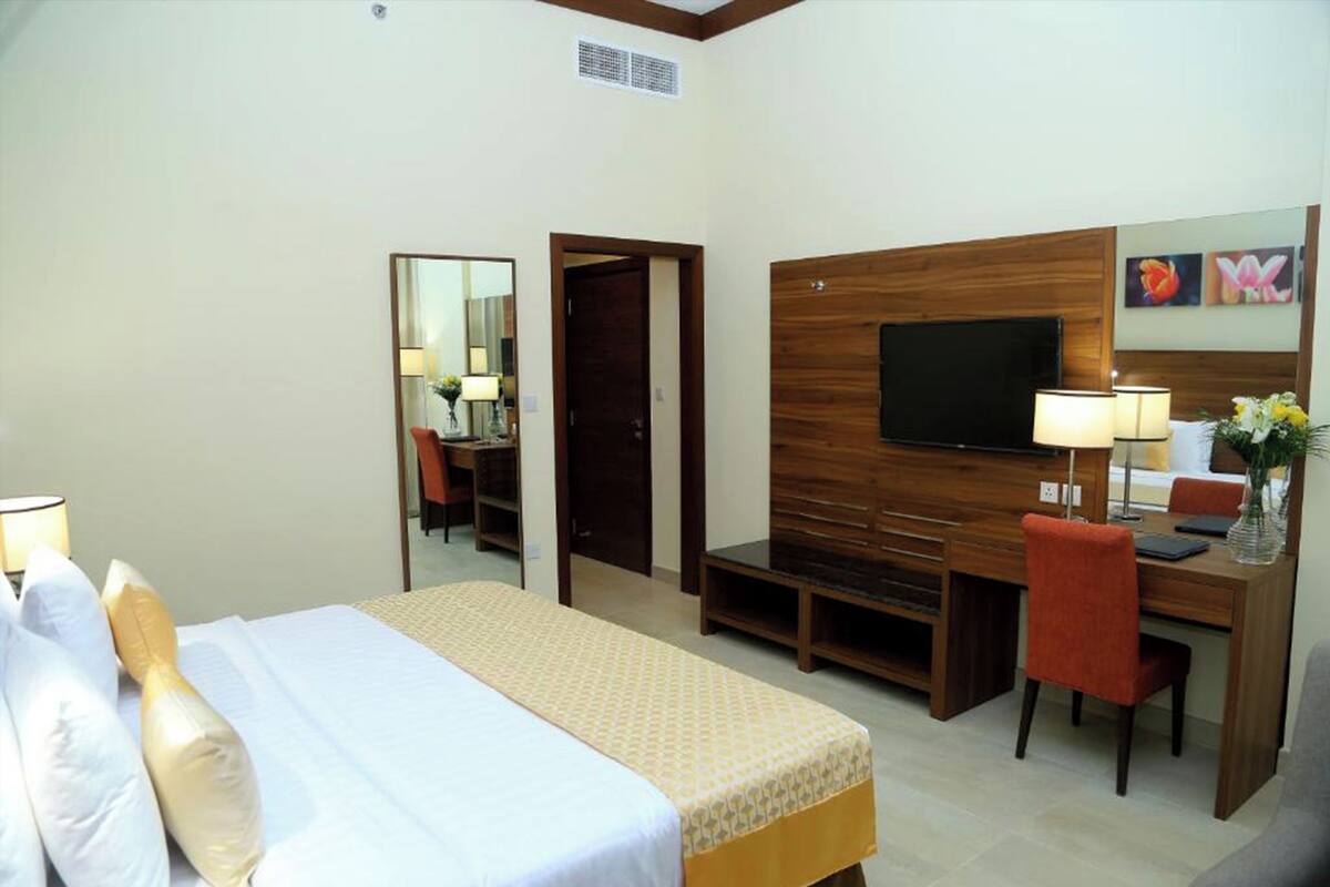 A hotel room with a bed, a desk with a chair, a television, and a mirror.