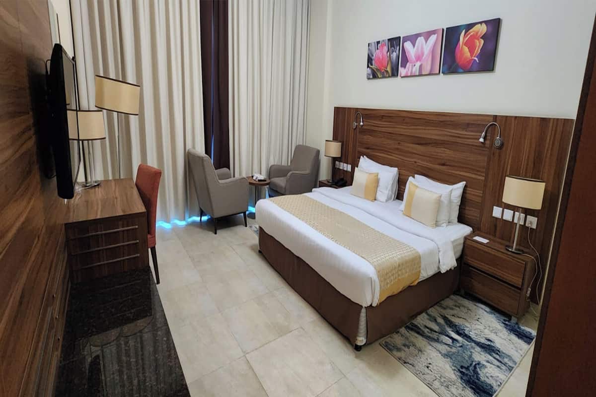 A hotel room with a large bed, two bedside tables, a desk with a chair, a TV, and a window with curtains.