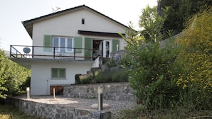 Una casa a due piani con un muro di sostegno in pietra, persiane verdi e un balcone.