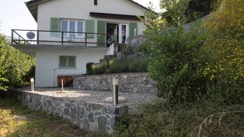 Ein zweistöckiges Haus mit einer Steinmauer, grünen Fensterläden und einem Balkon.