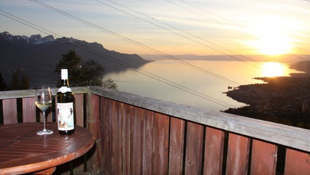 Un pontile in legno con un tavolo, una bottiglia di vino e un bicchiere, con vista su un lago montano al tramonto.