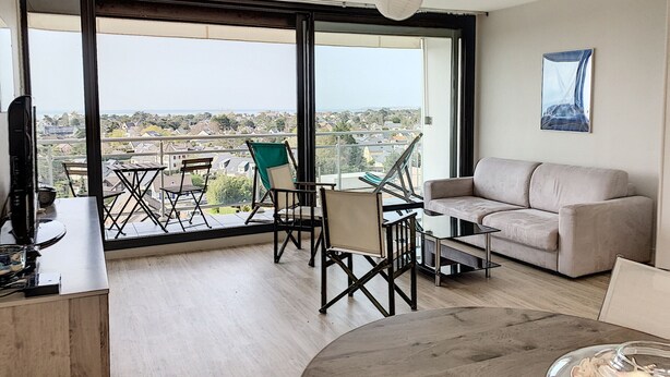 Un salón amplio con un gran ventanal, balcón, sofá y mesa de comedor.