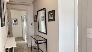 Un pasillo con una puerta blanca, una mesa de vidrio con un libro y cuadros en la pared.