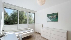 Una habitación con un ventanal grande, una cama, un escritorio y un radiador.