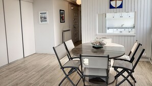 Un comedor con una mesa redonda, cuatro sillas, un bol de cristal sobre la mesa y una cocina visible a través de un umbral abierto.