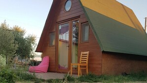 A small, triangular wooden cabin with a glass door and windows, surrounded by greenery. - Metis Bungalow (Ayvacik)