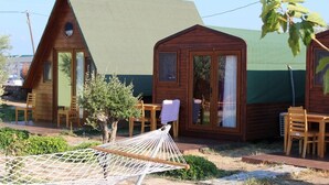 A wooden cabin with a green roof, a small porch with chairs, and a hammock. - Metis Bungalow (Ayvacik)