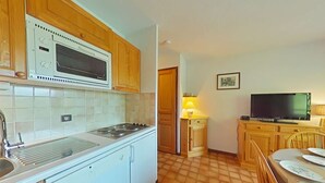 A compact kitchen with a stove, sink, and cabinets, a dining area with a table and chairs, and a television on a stand. - Cozy 2-Room Apartment for 5 with Ski Storage and Garage in Le Grand-Bornand (Le Grand-Bornand)