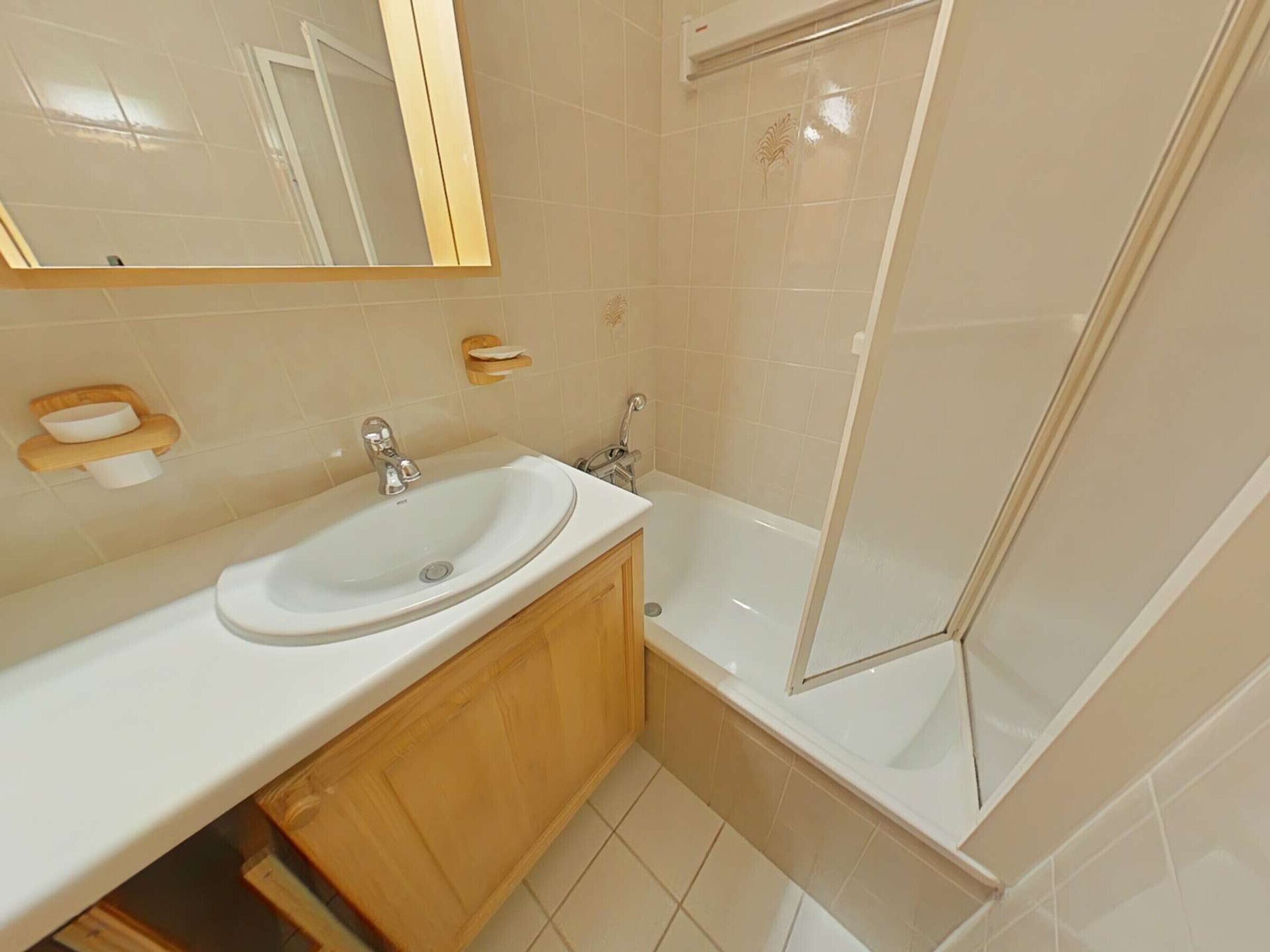 Un baño con lavamanos, espejo, tocador y ducha con mampara de vidrio.
