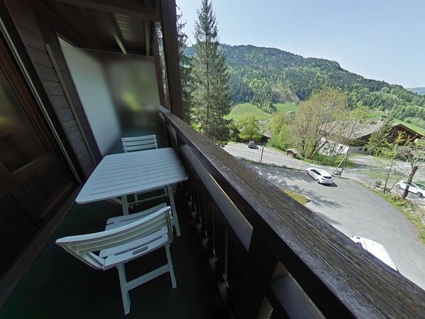 Un balcon avec une table et des chaises donnant sur une vallée où l’on aperçoit une route et des voitures garées.