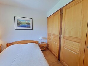 Ein Schlafzimmer mit Bett, Nachttisch, Lampe, Kleiderschrank und einem gerahmten Bild an der Wand.