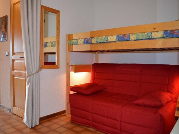 A room with a bunk bed, a red sofa, a wooden headboard, a mirror, and a curtain.