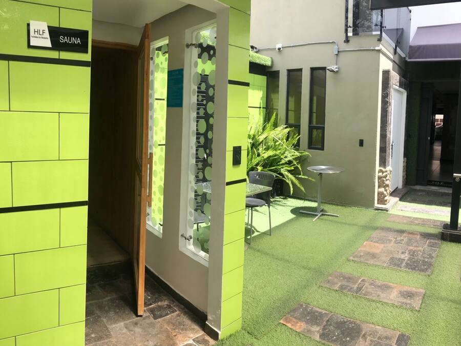 Área de spa com parede revestida de azulejos verdes, placa de sauna, janela com padrão de poás, uma pequena mesa e uma cadeira.