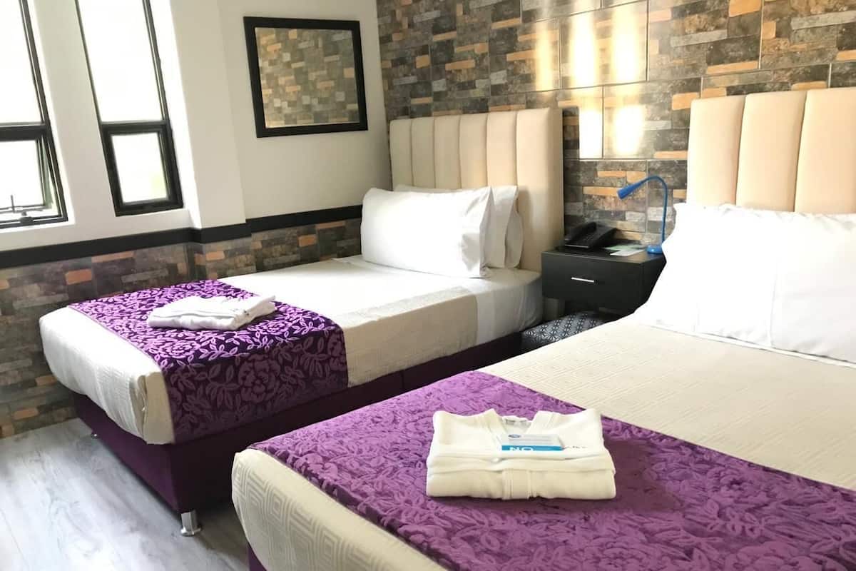 A hotel room with two beds, each with a purple bedspread and white pillows. There is a nightstand with a lamp and a framed picture on the wall.