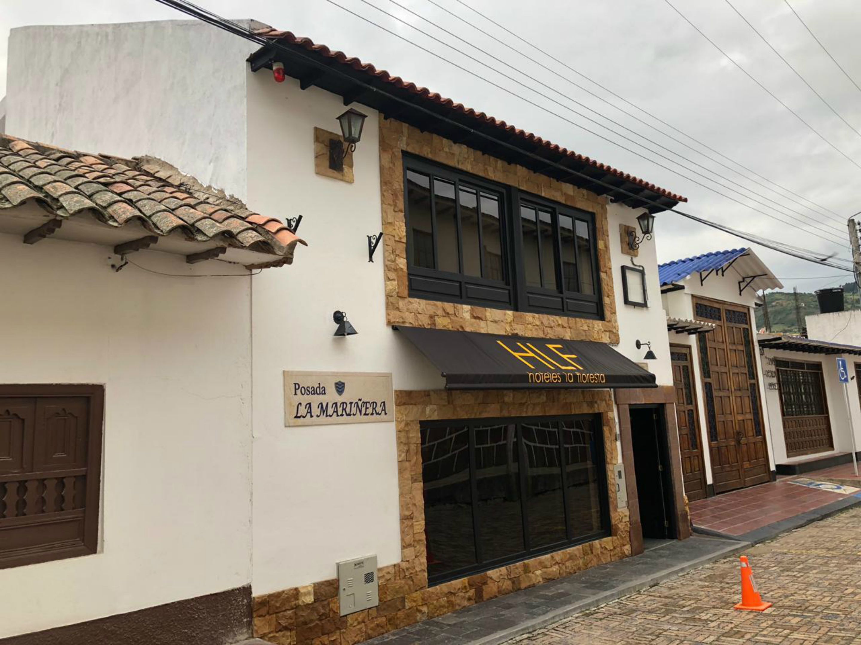 A two-story building with a sign for 'Posada La Marinería' and a black awning with 'HLE' logo.