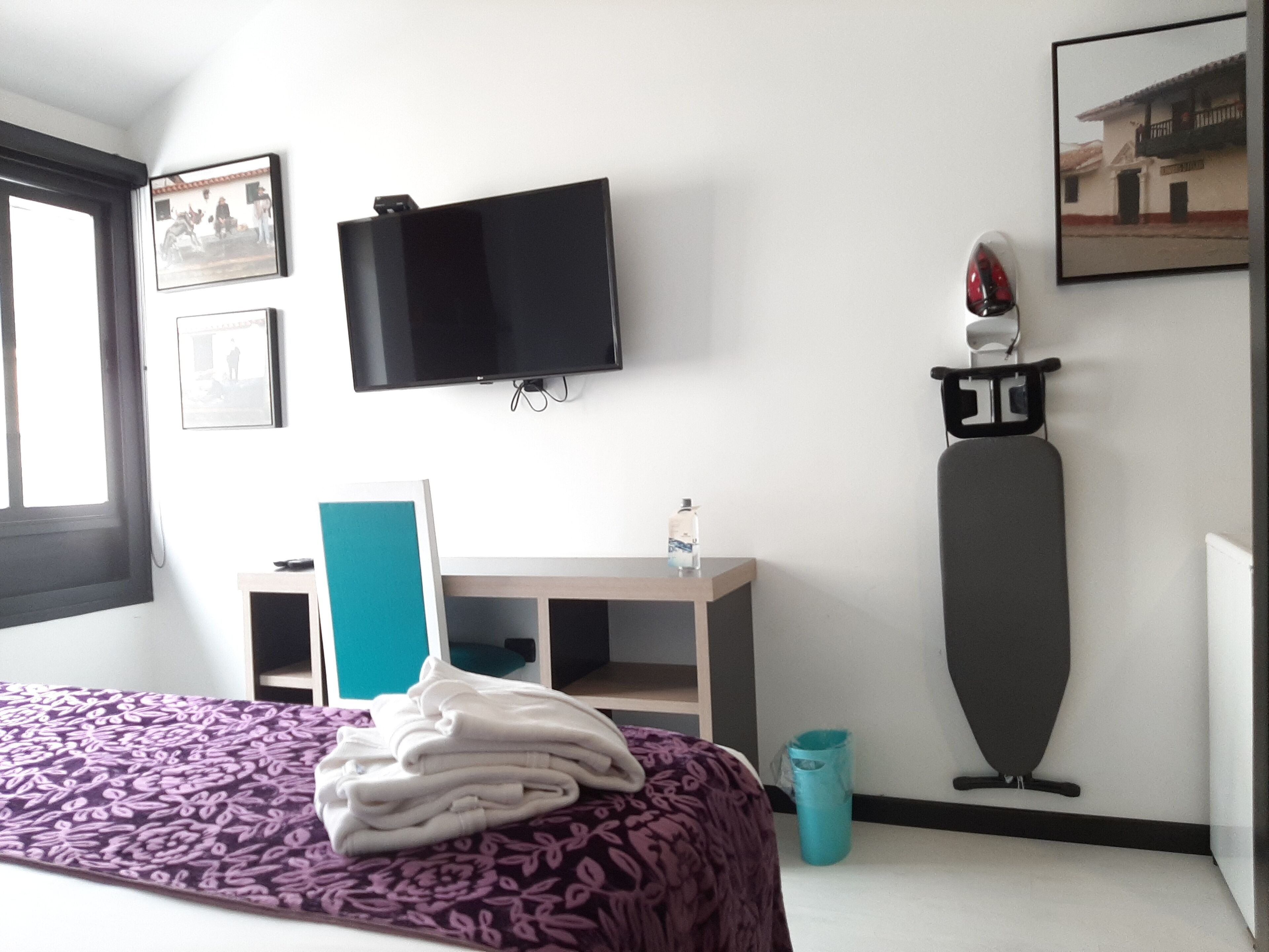 Une chambre d’hôtel équipée d’un lit, d’un bureau, d’une télévision, d’une planche à repasser fixée au mur et d’une fenêtre.
