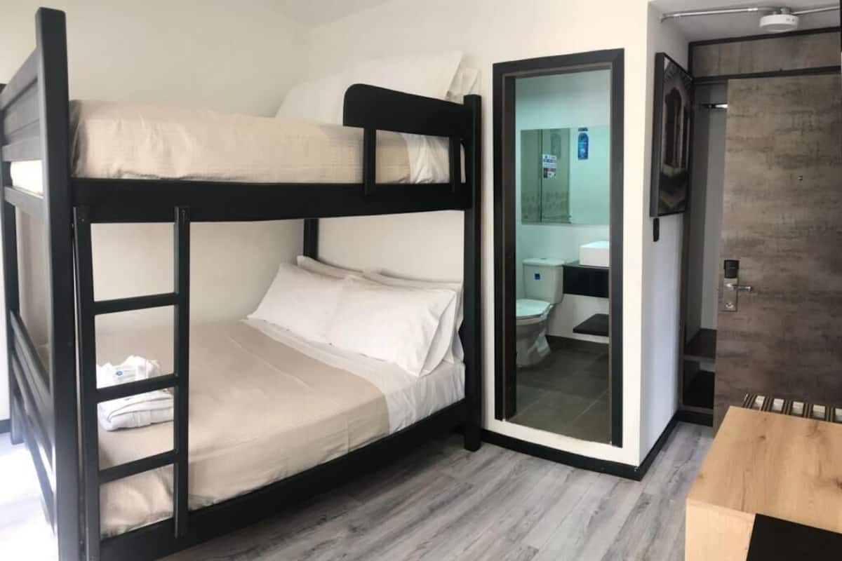 A bunk bed with a wooden frame, a small table, and a bathroom with a toilet and sink.