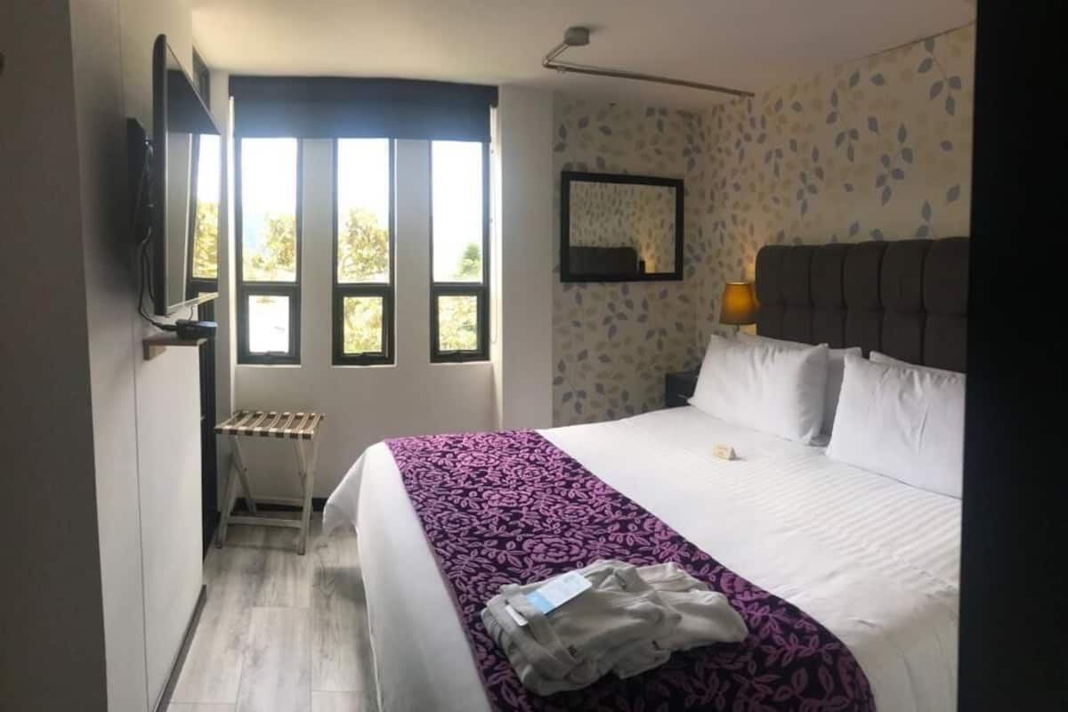 A hotel room with a bed, a window, a mirror, and a lamp.