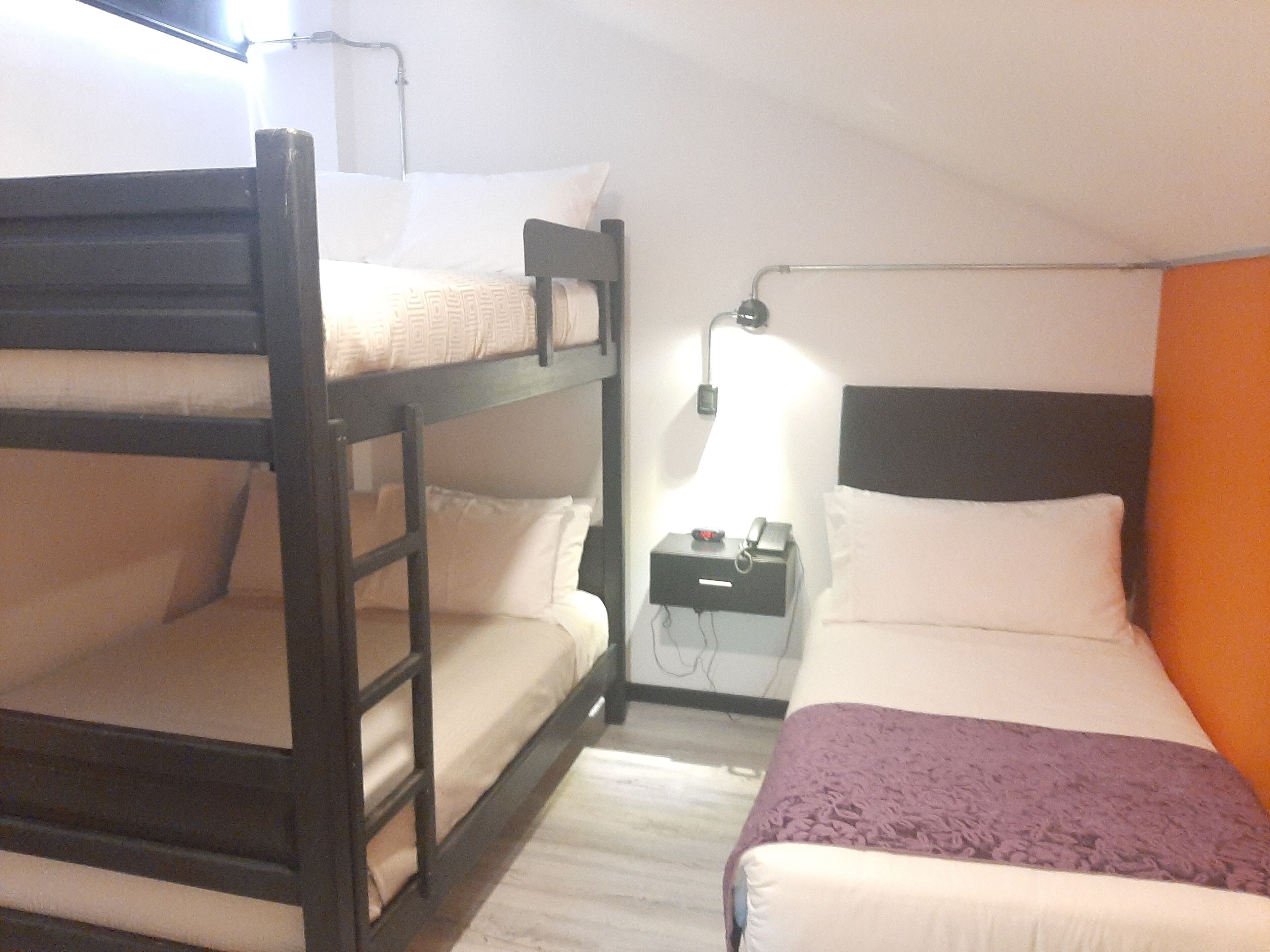 A bunk bed room with a nightstand, a lamp, and a bed with a purple blanket.