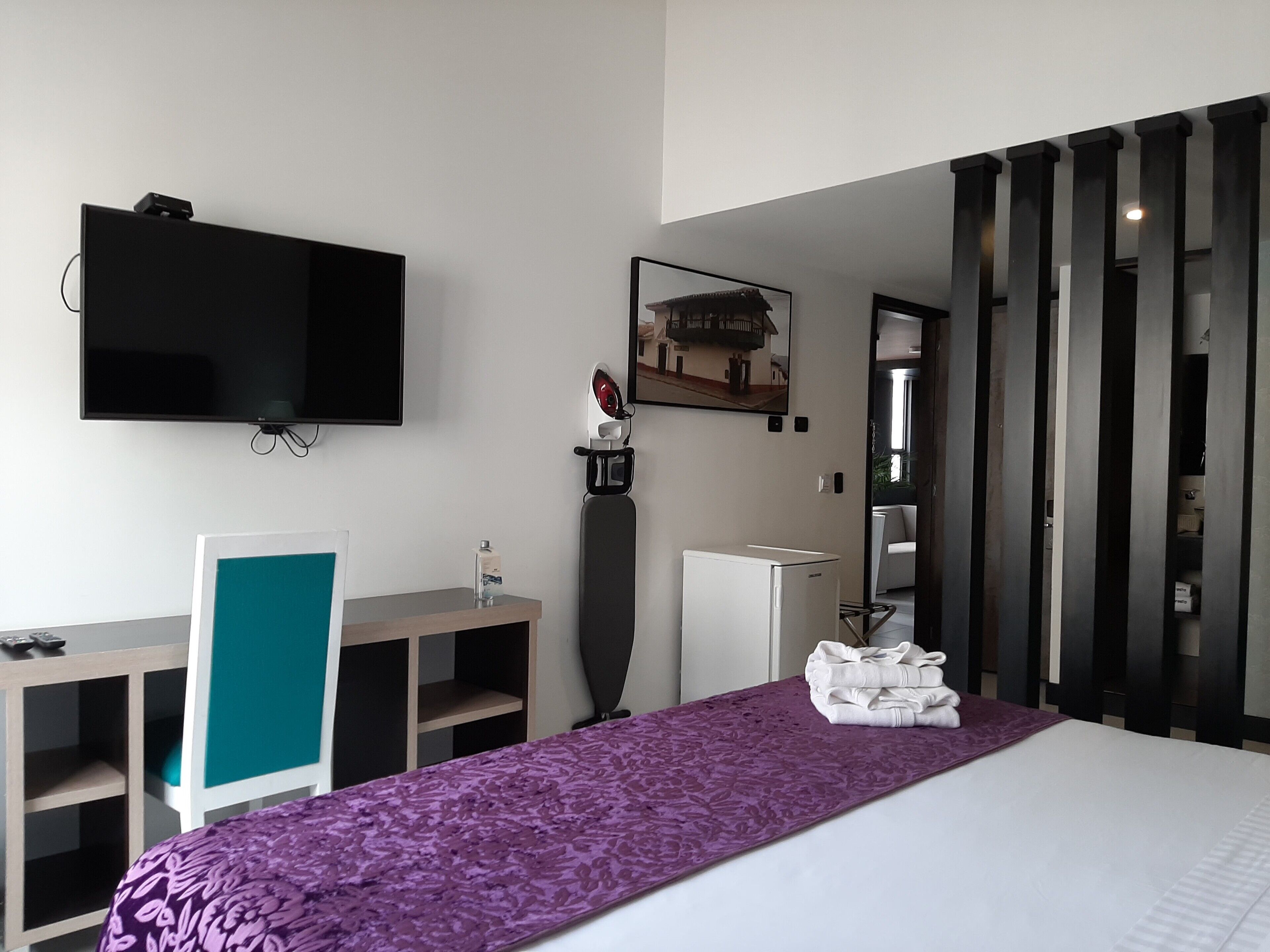 A hotel room with a bed, a desk, a television, a mirror, and a view of the outside.