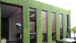 Un edificio con fachada verde, ventanas grandes y un pequeño espacio exterior con mesa y sillas.