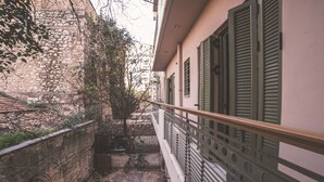 Une petite cour bordée d’un mur de pierre, avec un vélo et un balcon aux volets verts.