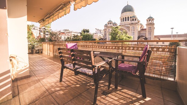 Un balcon doté d’un banc et d’une table en bois, offrant une vue sur un bâtiment historique surmonté de coupoles.