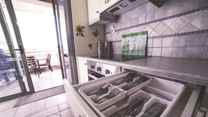 Une cuisine dotée d’un tiroir contenant des ustensiles, d’un crédence carrelée et donnant sur le balcon extérieur.