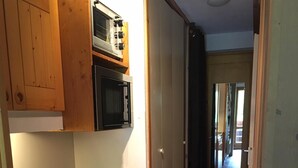 Cocina compacta con armarios de madera, microondas, estufa y lavavajillas.