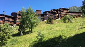 Un edificio de varios pisos con balcones, rodeado de vegetación y montañas al fondo.