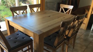 A wooden dining table with cushioned chairs, a tiled floor, and a view of greenery outside. - House near the African reserve (Sigean)