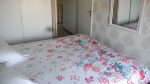 A bedroom with a floral bedspread, a door with a mirror, and a wardrobe. - House near the African reserve (Sigean)