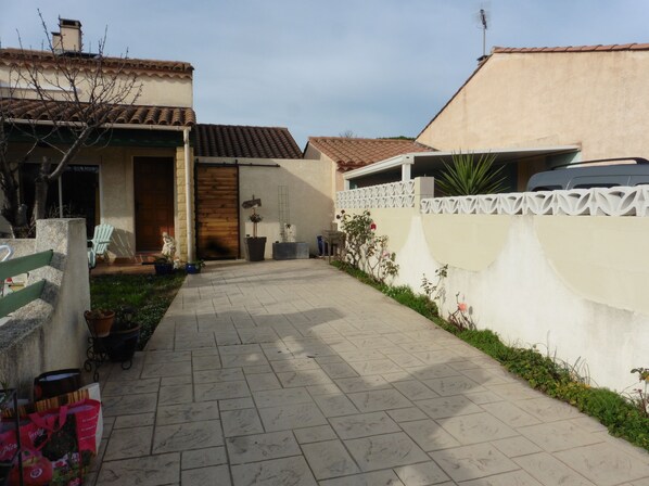 Un camí pavimentat que condueix a una casa amb una porta de fusta i una tanca blanca.