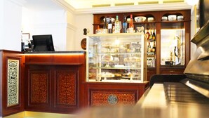 Un espace bar avec un piano, une vitrine réfrigérée où sont présentés des desserts, et des étagères remplies de bouteilles.