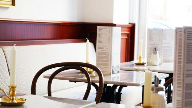 L’intérieur d’un restaurant avec des banquettes en bois, des tables blanches et des chandeliers.
