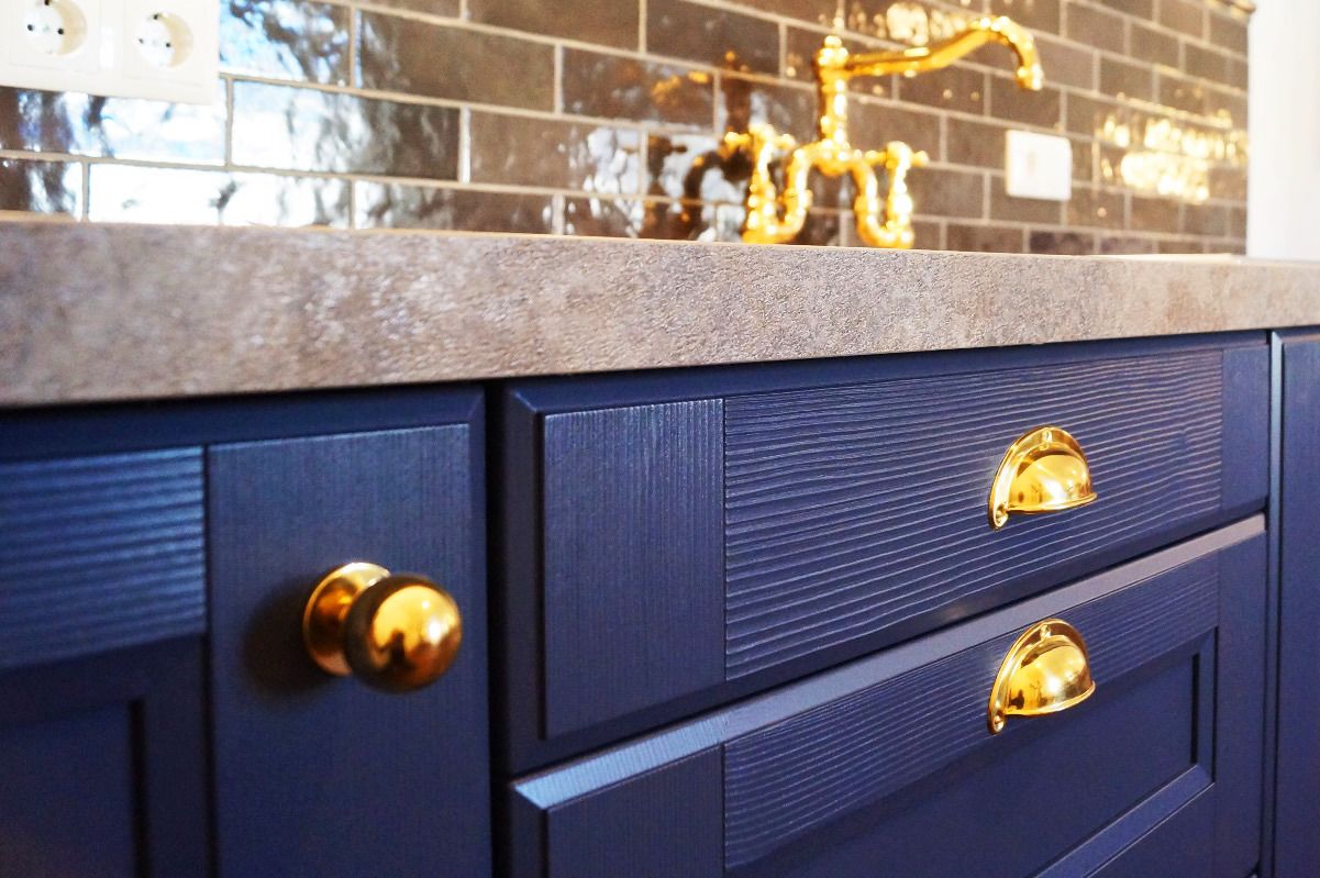 A dark blue cabinet with gold handles and a tiled backsplash.