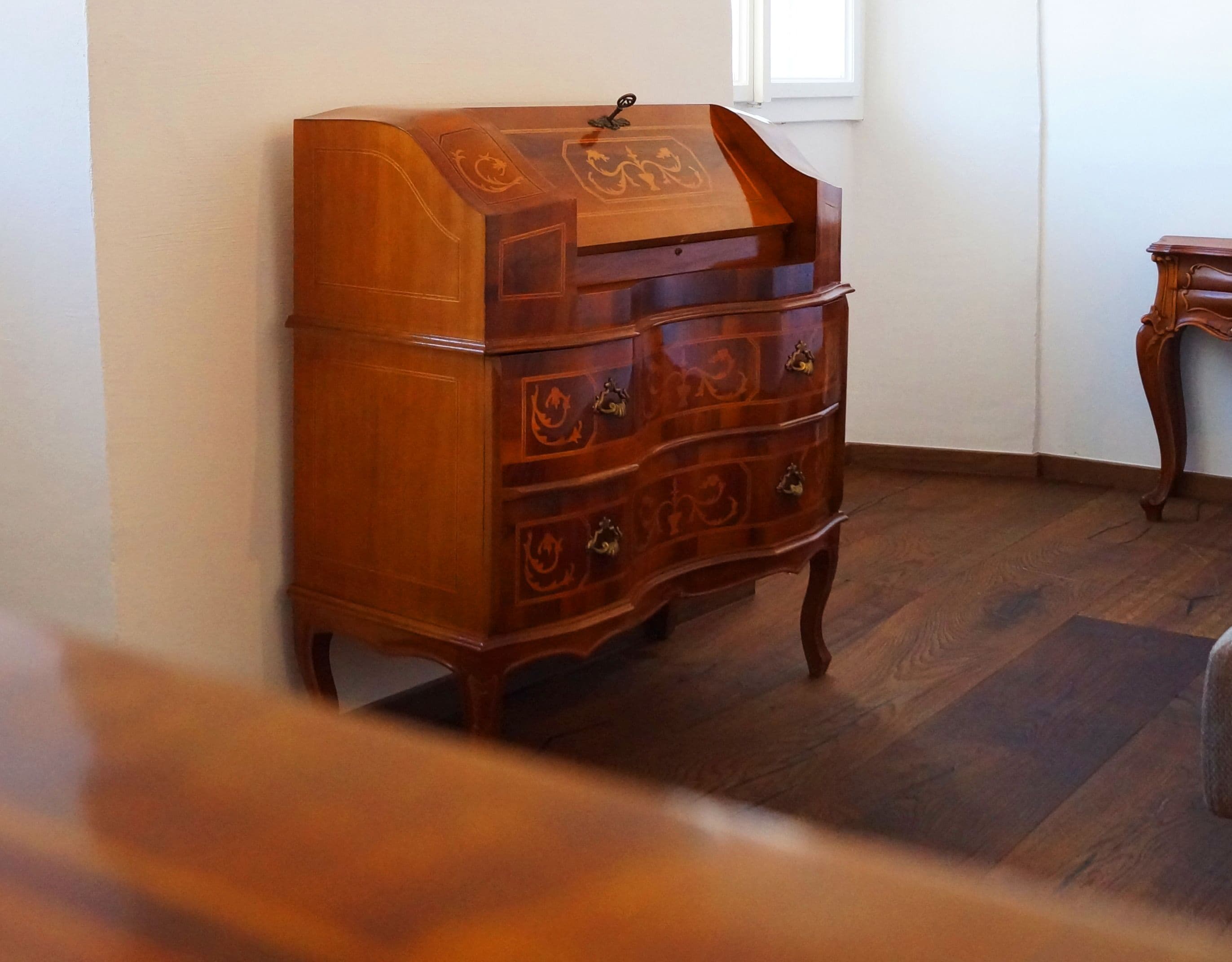 A wooden chest of drawers with ornate carvings, positioned against a wall in a room with wooden flooring.