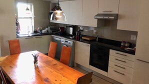 A modern kitchen with white cabinets, a wooden dining table, and a pendant light. - Summer vacation in Cape Town, South Africa (Plumstead)