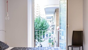 A bedroom with a bed, a chair, and a balcony with a view of a city street and buildings. - Riviera Luxury Suites B&B (Naples)